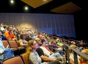 A group of people seated in a church sanctuary, attentively facing the front. Sound panels from ATS Acoustics are strategically placed on the walls to reduce echo, ensuring clear sound throughout.